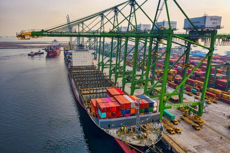 Aerial view of a cargo ship docked at New Priok Container Terminal, Jakarta, showcasing vibrant logistics activity.